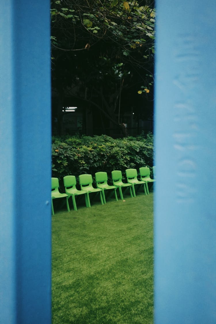 Plastic Green Chairs Aligned In The Lawn Beside The Bushes