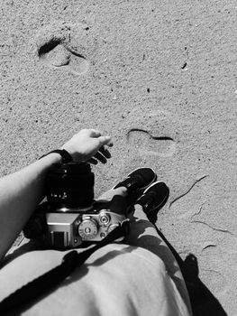 Person with camera walking on sandy beach, capturing footprints.