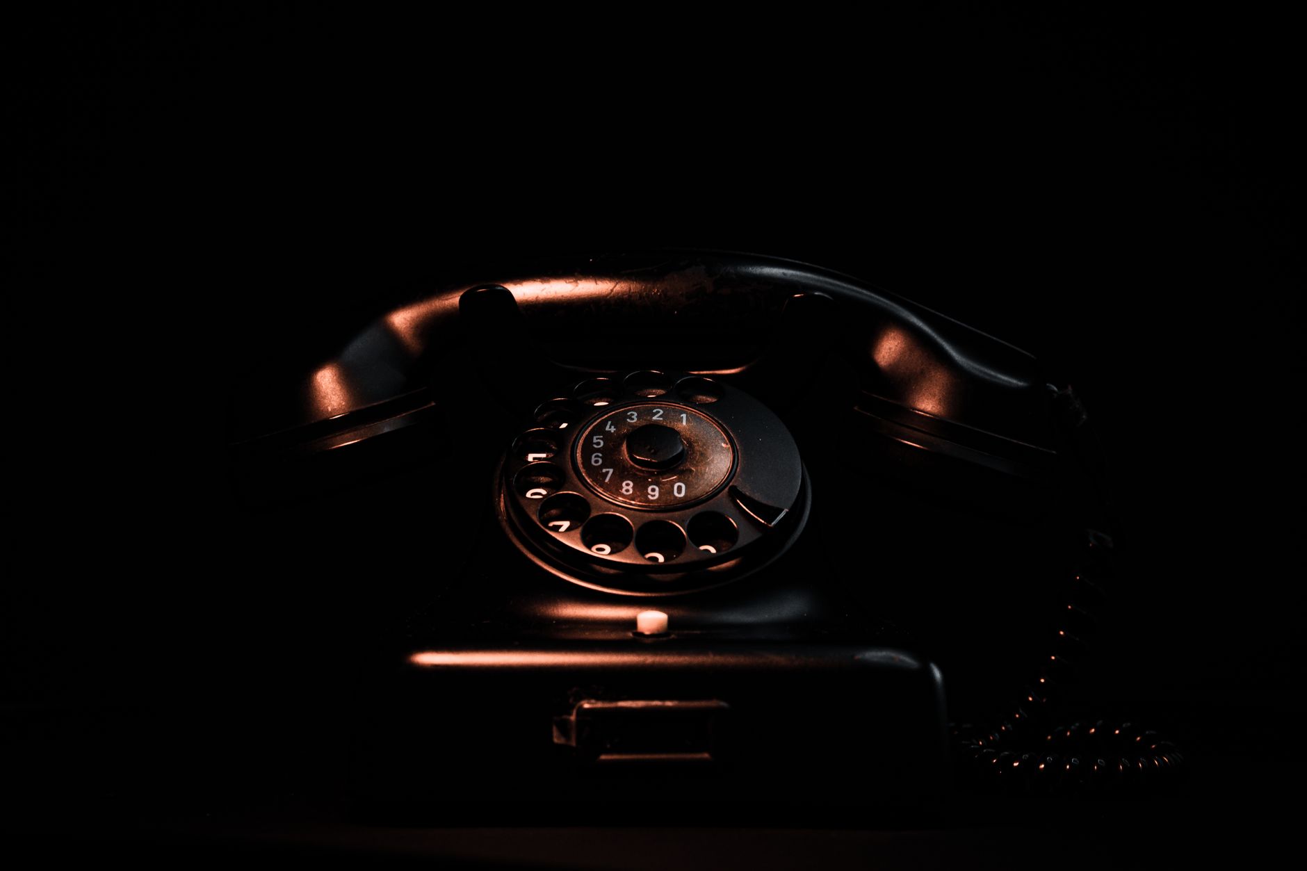 Vintage black rotary phone in a dark setting highlighting its classic design and retro appeal.