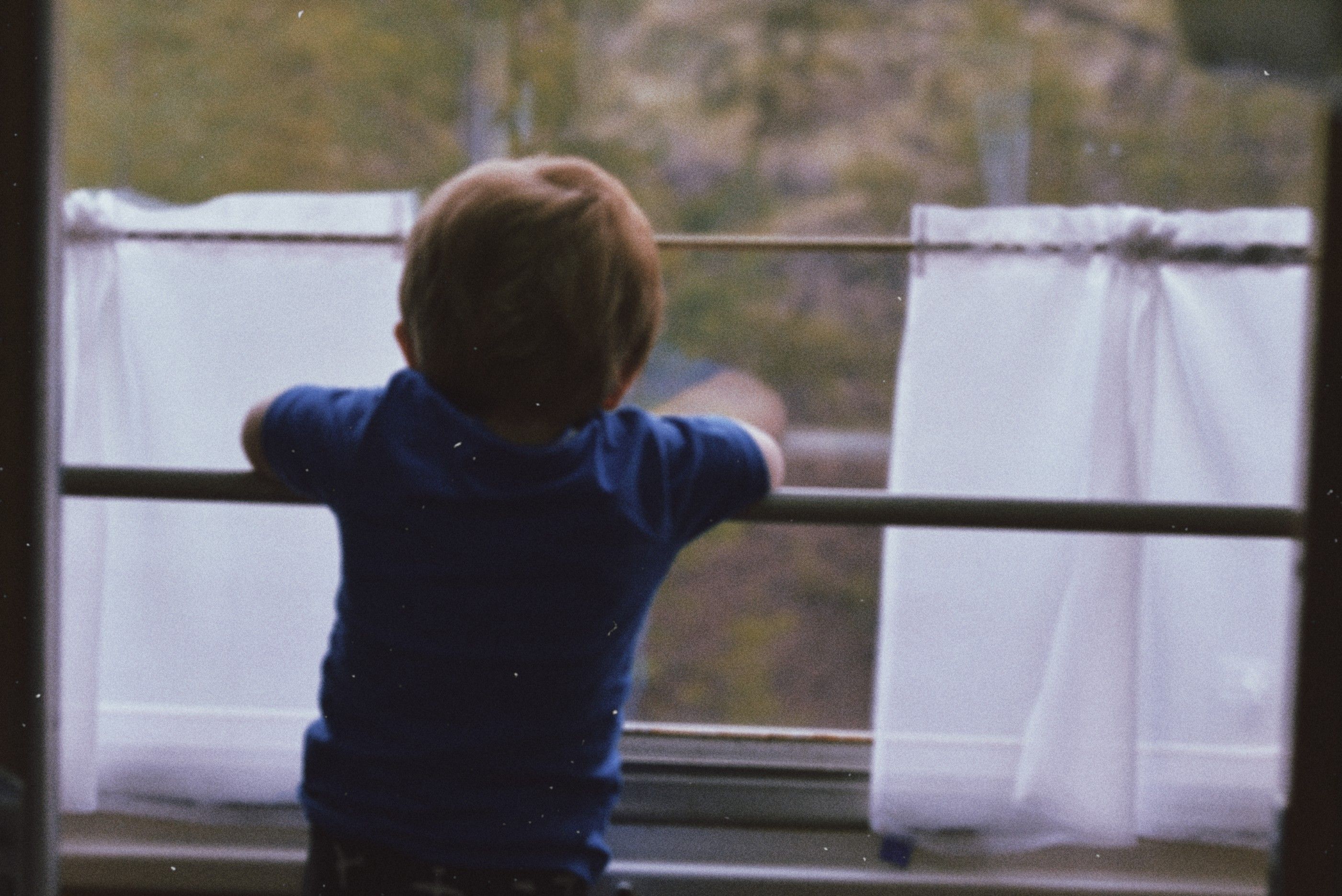 A young child leans against a window, exploring the outdoor world with curiosity.