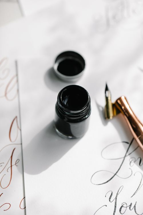 Free Close-up of a fountain pen and ink bottle on calligraphy paper, ideal for artistic themes. Stock Photo