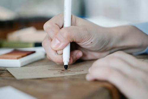 Free A close-up of a hand writing elegantly on paper using a black marker indoors. Stock Photo