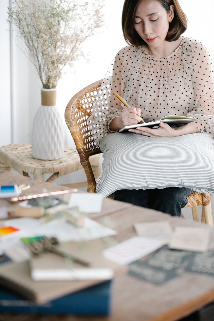 A Woman In A White And Black Polka Dot Shirt Writing On A Notebook