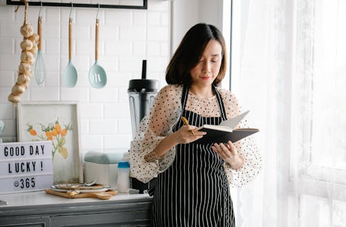 Free A Woman in an Apron Holding a Journal in a Kitchen Stock Photo