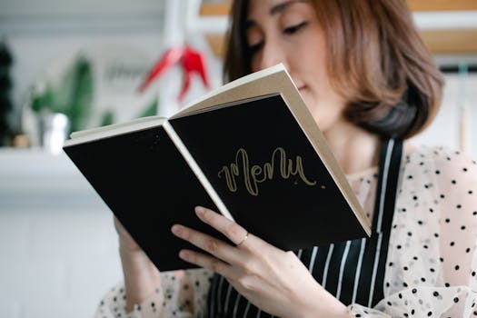 A chef in a polka dot blouse holds a menu book in a stylish restaurant, ready to present the dishes.
