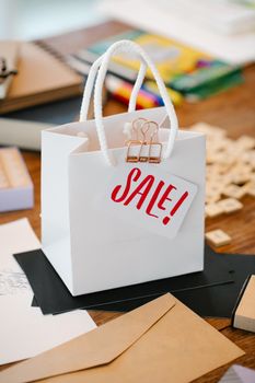 A white paper bag featuring a 'Sale!' tag on a wooden desk with stationery items.