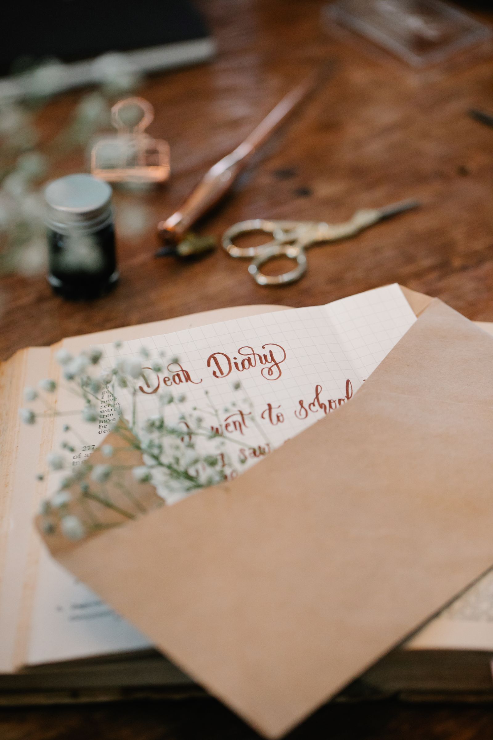 A handwritten note tucked into a kraft envelope on a wooden desk beside ink and scissors