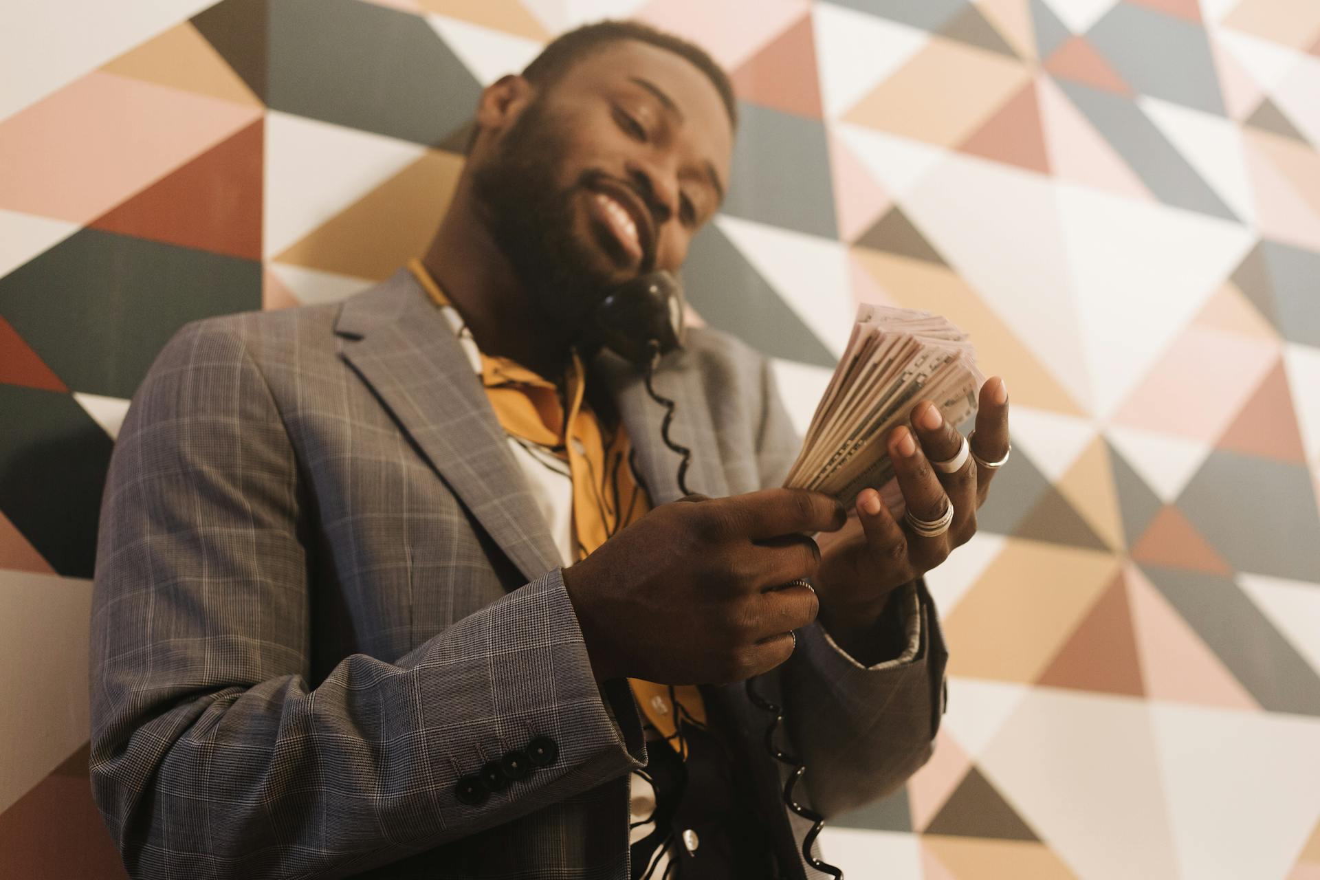 Smiling businessman in a suit holding cash while talking on a landline phone.