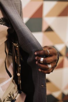 Close-up of a hand adorned with rings adjusting a jacket against a geometric background.