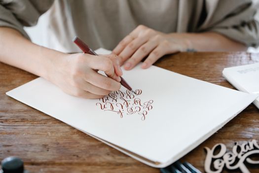 A person practicing calligraphy on paper with a pen, showcasing beautiful lettering.