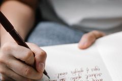 Close-up of a person writing calligraphy in a journal with a pen on a lined notebook.