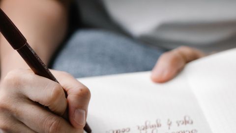 Close-up of a person writing calligraphy in a journal with a pen on a lined notebook.