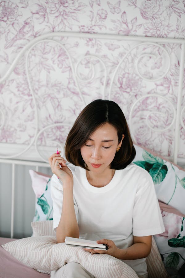 Woman Sitting on a Bed and Writing in a Notebook
