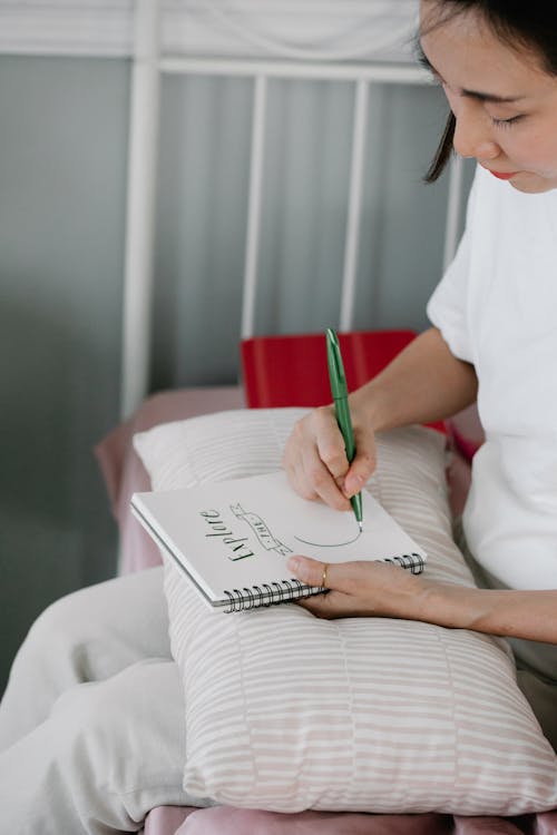 Free Woman in White Shirt Writing on White Notebook Stock Photo