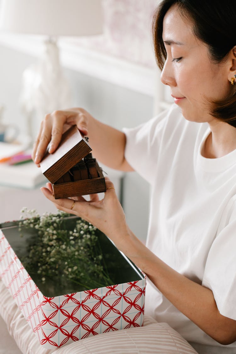 A Woman Opening A Wooden Box Over A Box Of Flowers