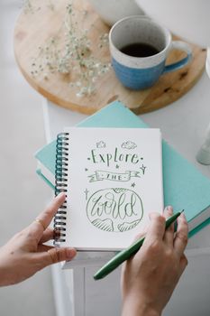 Closeup of hands writing in a notebook with a coffee cup nearby, a calm creative setting.