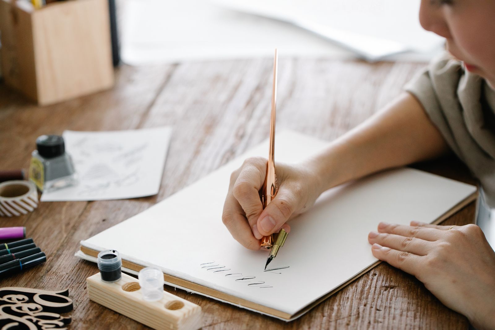 Person practising calligraphy at a wooden table, photo by Katya Wolf on Pexels