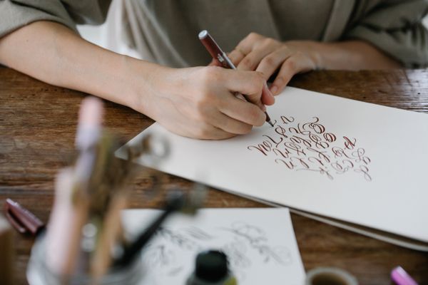 Hands practicing calligraphy on white paper — photo by Katya Wolf on Pexels