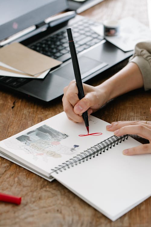 Close-Up Shot of Person Writing on Spiral Notebook