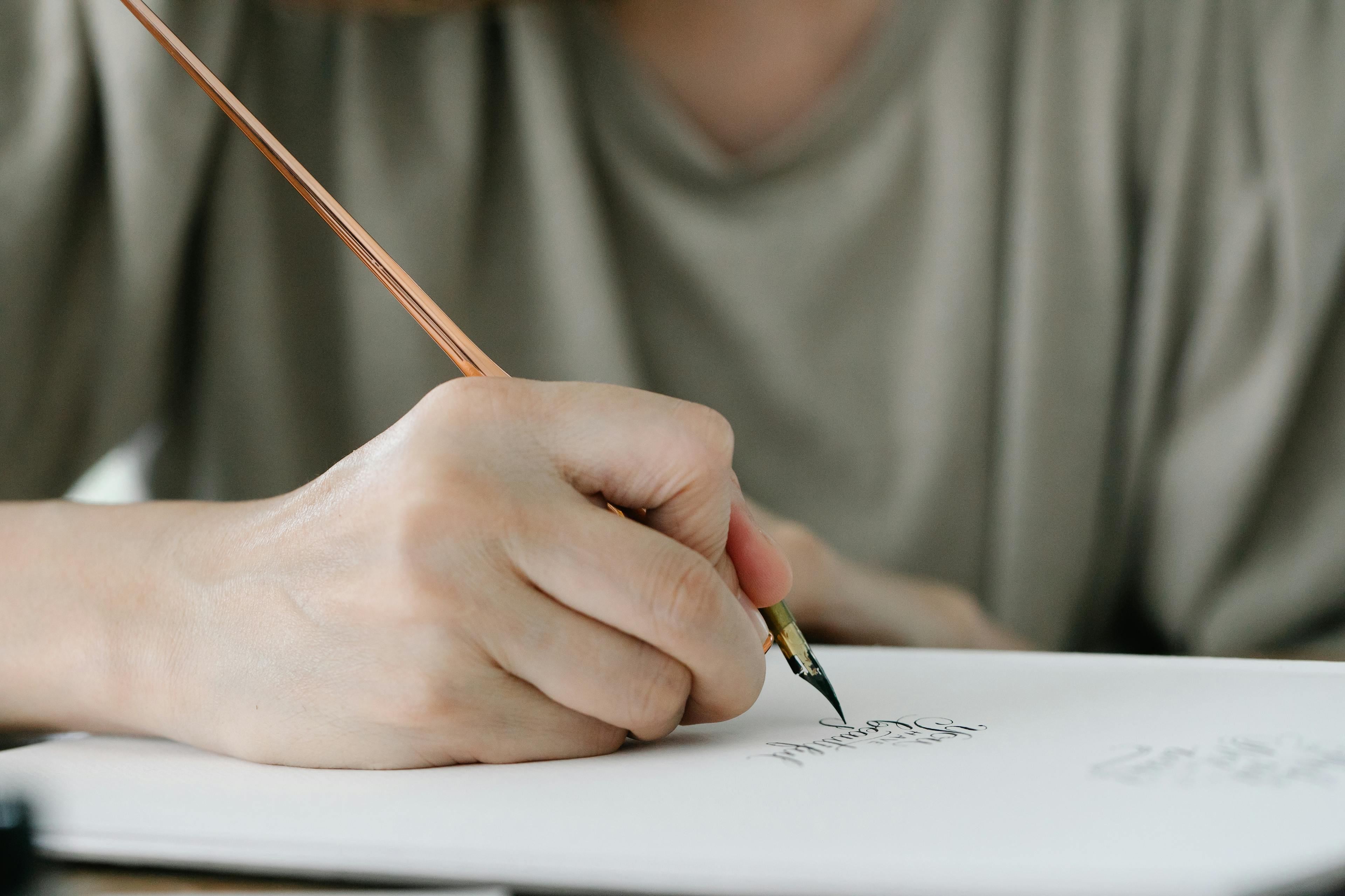 Person practicing script writing on a wooden desk with a pen