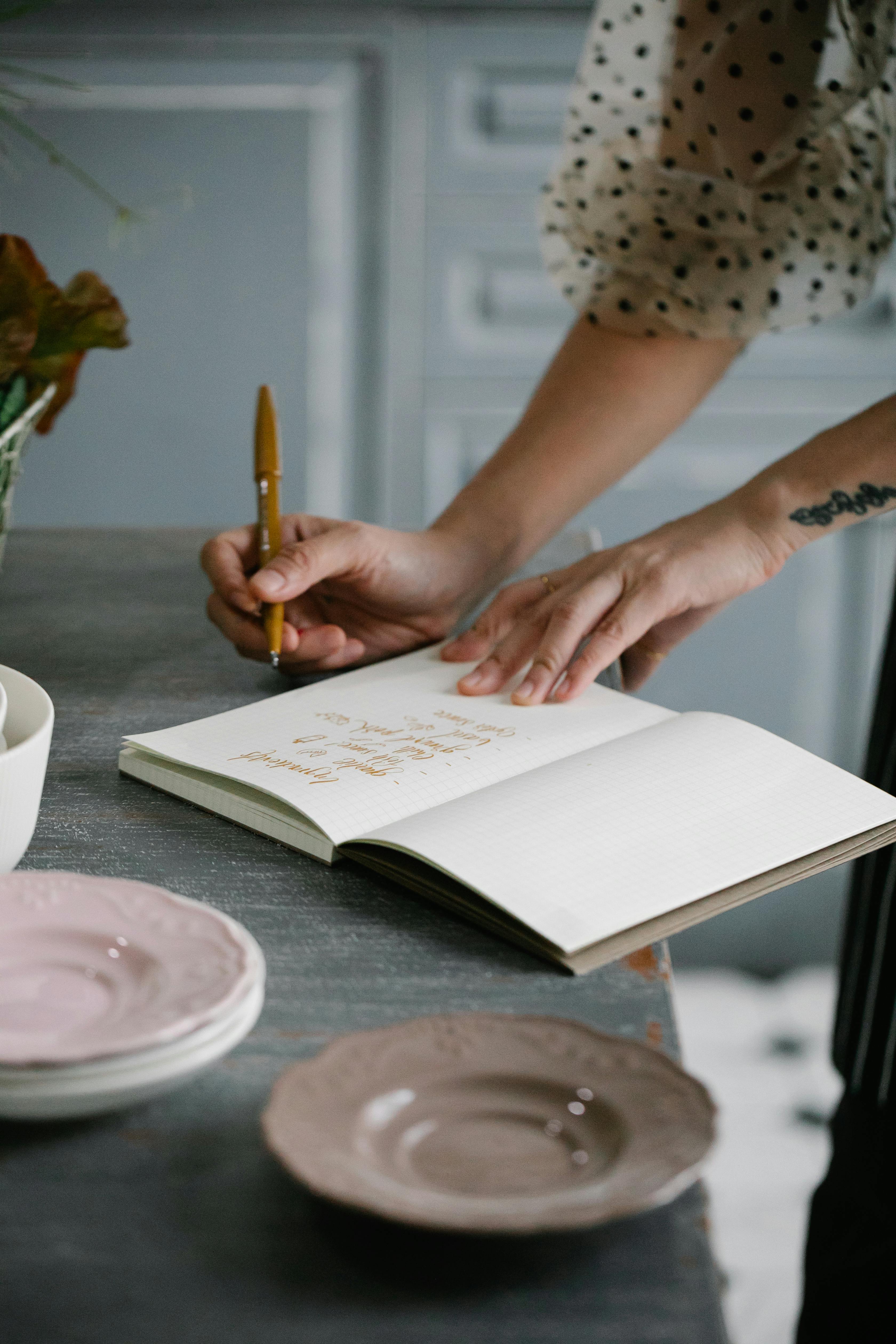 A close-up of a person writing notes in a small notebook while tasting food.