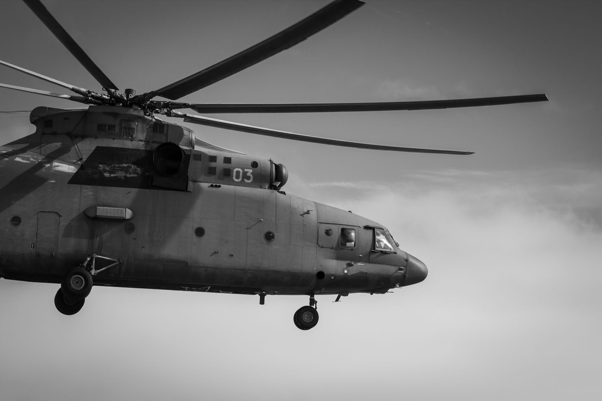 A detailed black and white image of a helicopter in flight against cloudy skies.
