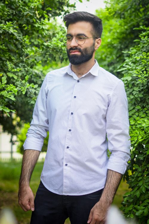 Free Portrait of a young man with a beard standing outdoors in foliage, wearing glasses. Stock Photo