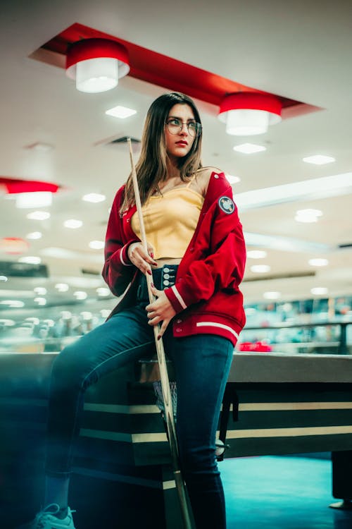 Photo of a Woman Holding a Cue Stick while Sitting on a Pool Table