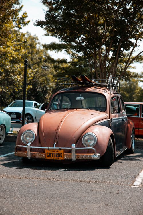 Free An aged Volkswagen Beetle parked in a sunny outdoor setting with trees in the background. Stock Photo
