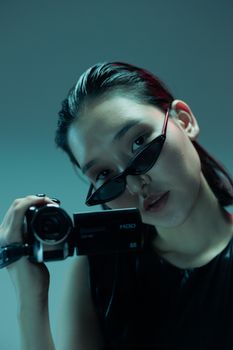 Close-up of an adult holding a camera, wearing sunglasses indoors.