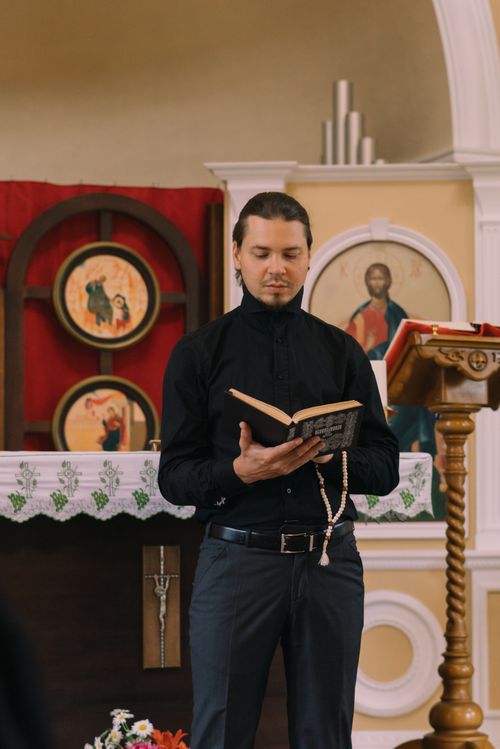 Free Priest in black attire reading a bible with prayer beads during church ceremony. Stock Photo