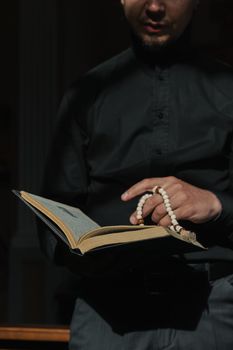 Close-up of a man reading a book with prayer beads in low light, highlighting spirituality and contemplation.
