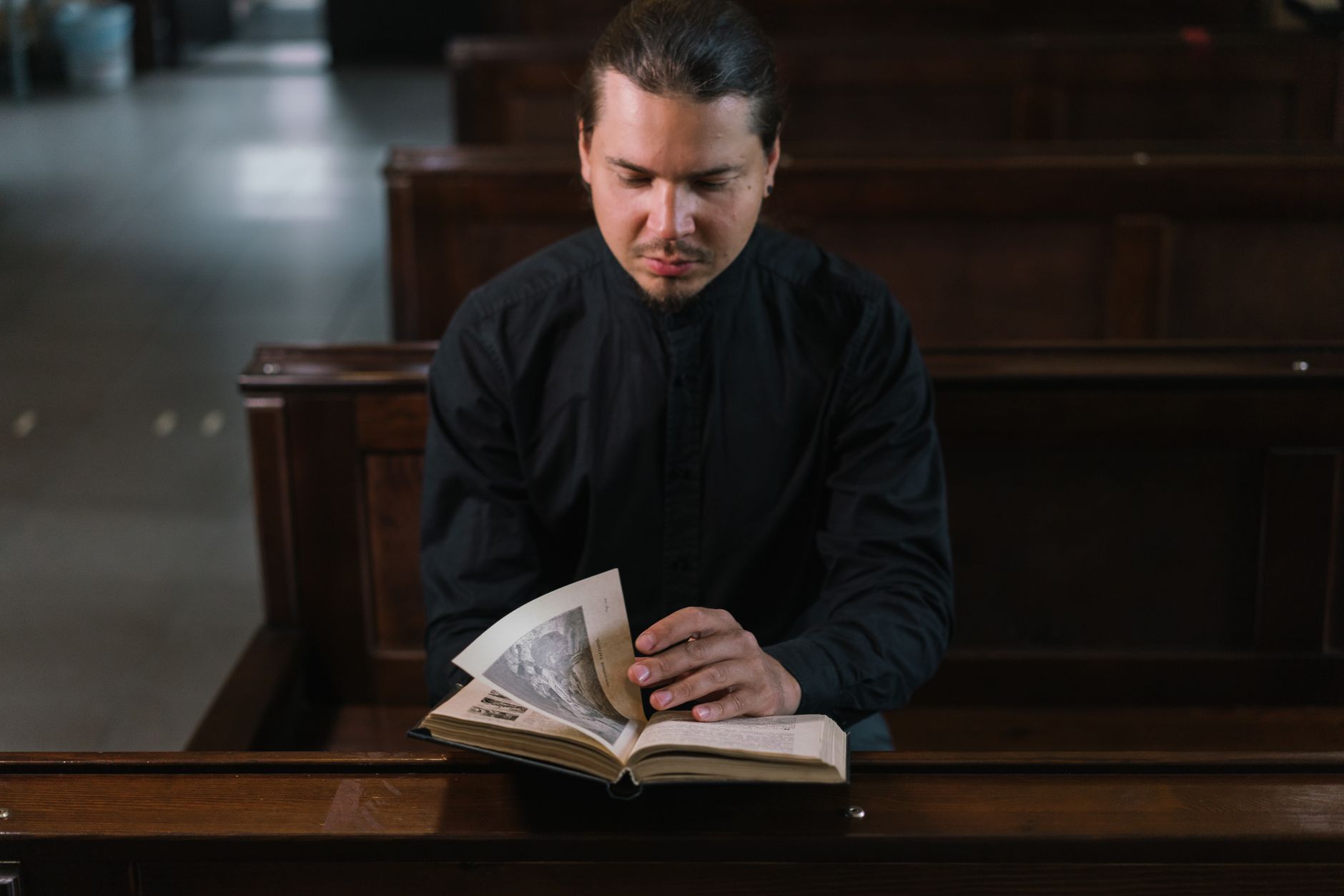 A man dressed in black reads a Bible inside a church, conveying spirituality and faith.