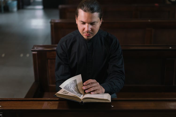 Man In Black Clothes Inside A Church Reading A Bible