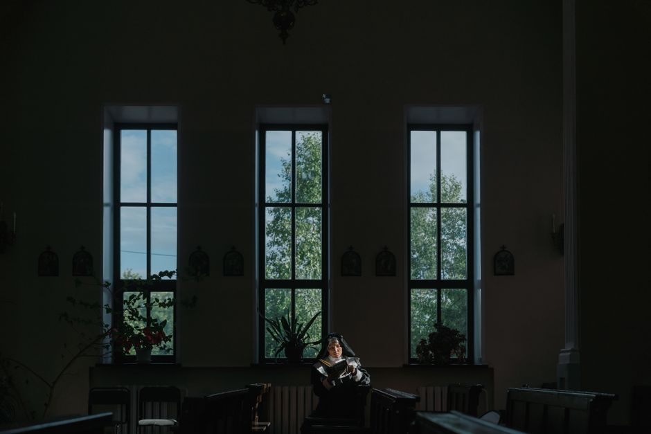 A nun reads quietly in a dimly lit church, illuminated by soft window light, epitomizing peaceful spirituality.