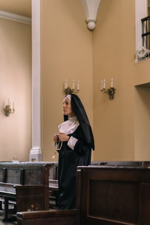 Free A nun in a black habit prays with a rosary in a serene church setting. Stock Photo