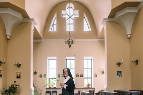 Free A nun in traditional habit is praying inside a beautifully lit church with a serene interior. Stock Photo