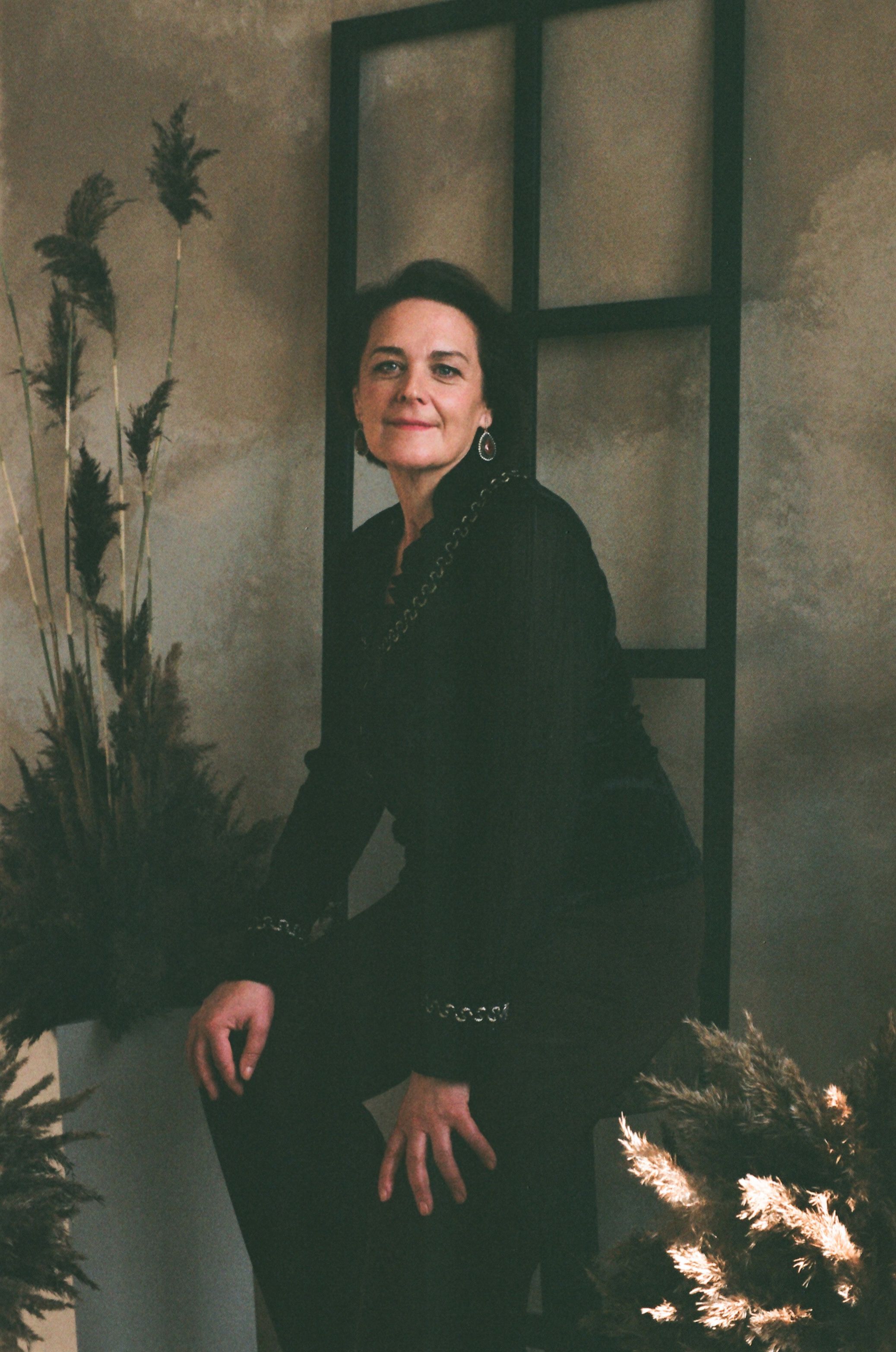 Portrait of a woman sitting elegantly against a modern backdrop with plants.