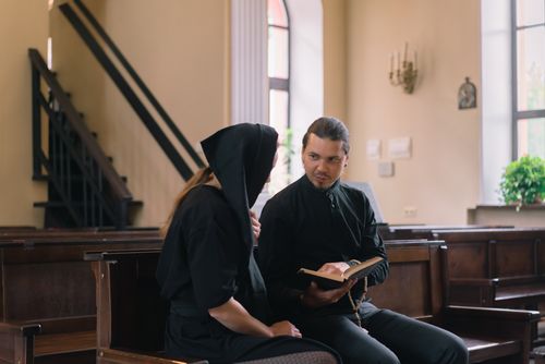 Free A priest and a woman in black clothing hold a religious discussion inside a church. Stock Photo