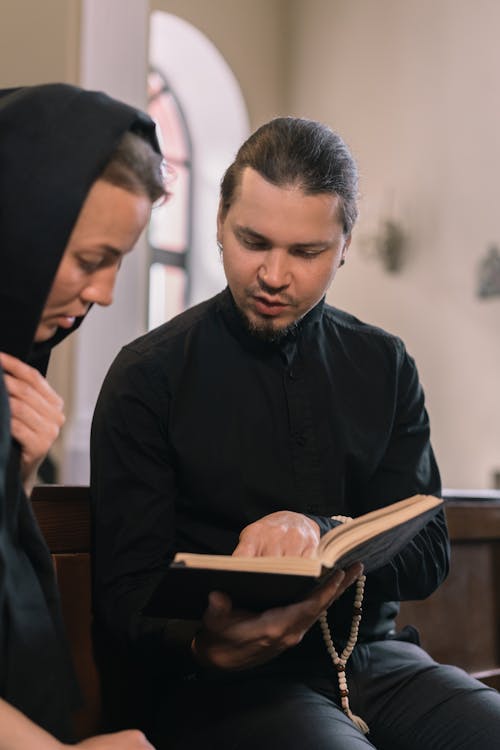 A Man in Black Long Sleeve Shirt Holding a Rosary and Reading a Bible