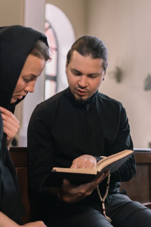 Free A priest guiding a parishioner through the Bible inside a church setting. Stock Photo