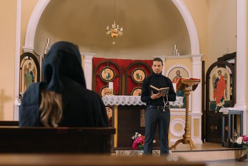 Free A priest reading scripture in a church with a person in the pews, emphasizing spirituality. Stock Photo