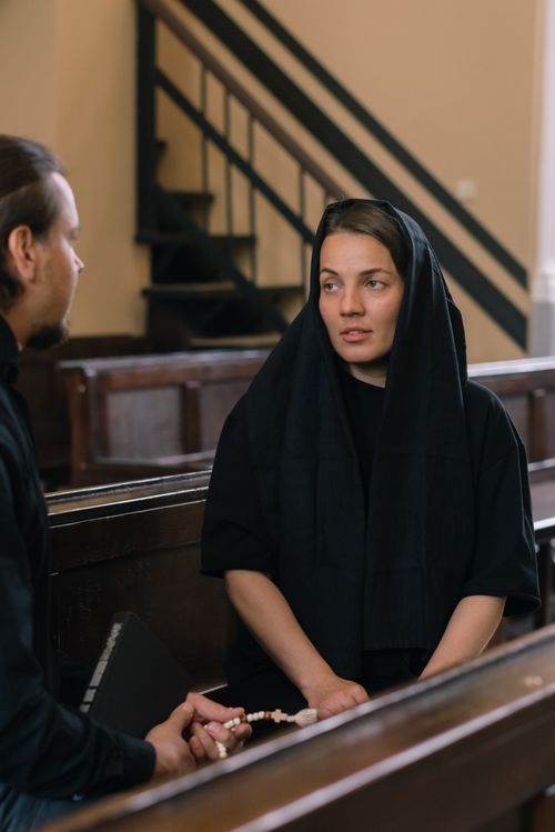 Free A woman conversing in a church setting with a man, holding a rosary. Stock Photo
