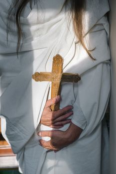 A person in a white robe holds an ornate wooden cross, symbolizing faith and spirituality.