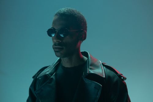 Free Moody portrait of an African American man wearing sunglasses and a leather jacket, against a cool blue background. Stock Photo