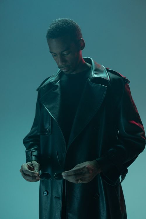 Free A stylish man in a leather coat adjusts his sunglasses, captured in a conceptual cyberpunk-inspired studio shoot. Stock Photo