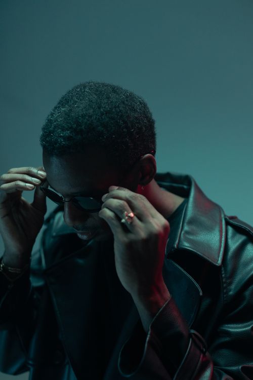 Free Stylish man in black leather jacket adjusting sunglasses in a moody light. Stock Photo