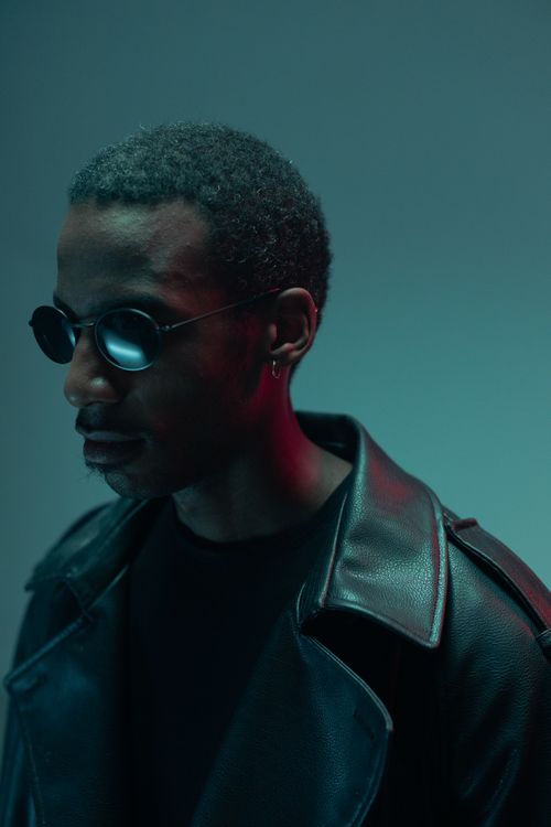 Free Portrait of a stylish African American man wearing sunglasses and a leather jacket in moody lighting. Stock Photo