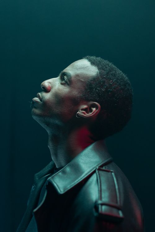 Free Side profile of a man in a black leather jacket looking contemplatively upward under dramatic lighting. Stock Photo