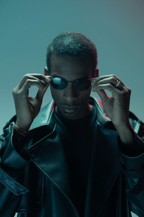 Free Portrait of a fashionable man wearing sunglasses and a leather coat, showcasing a modern style. Stock Photo